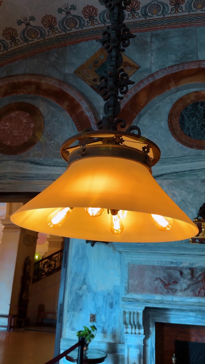 Lampada a sospensione a cupola vintage con lampadine Edison in una stanza di marmo. Primo piano di una lampada a cupola in vetro smerigliato con lampadine a luce calda contro una parete di marmo con murales decorativi.