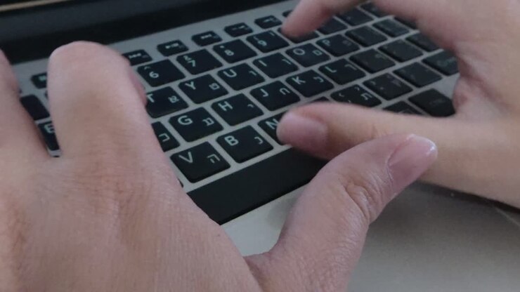 Side angle close-up of woman's hands typing on laptop at home office desk.
