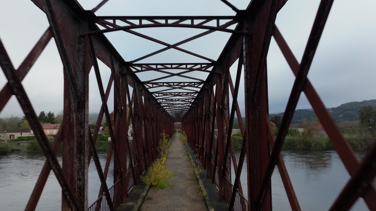 Interior perspective of the Pont du Garrit metal framework showing the pedestrian walkway. Symmetrical drone shot moves through the rusted steel trusses of this Eiffel-style engineering landmark