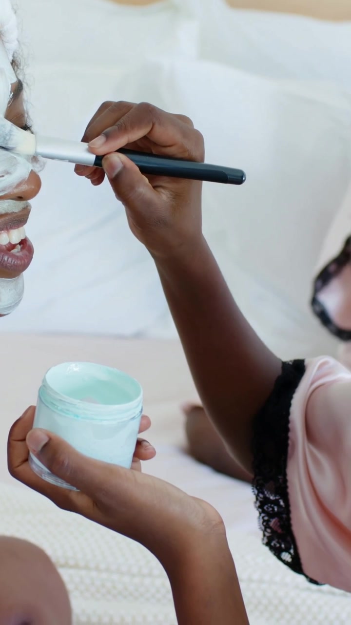 Vertical video: Picking up mint jar, youth in pink robe applying mask on mother on bed for bonding