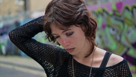 close up outdoor fashion portrait of young alternative style woman with eyebrow piercing in front of graffiti covered wall in london city street uk in real time 3