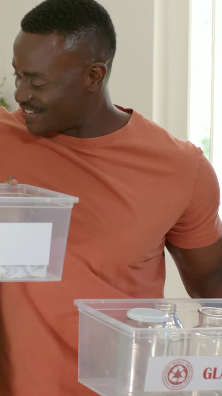 Vertical video: Holding bin at chest, man in orange tee checking GLASS bin at counter, sorting