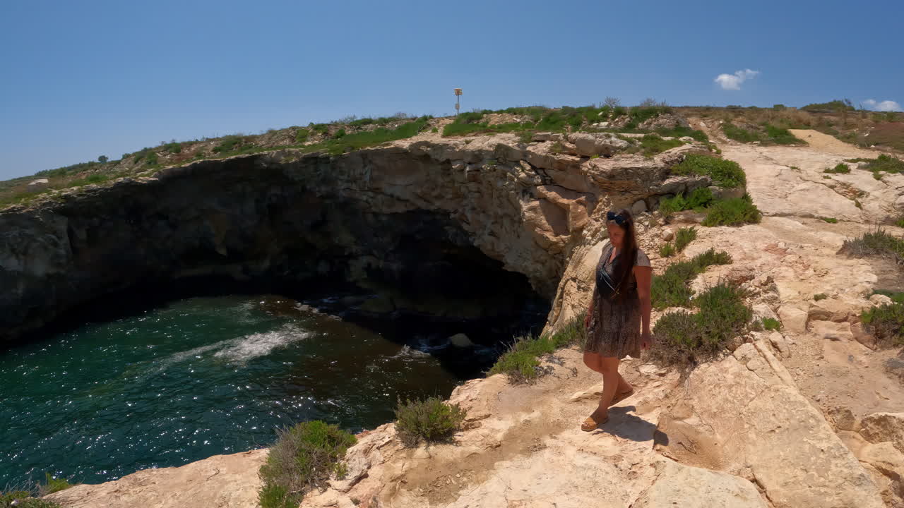 한 여인이 몰타 섬의 바물에 의해 침식된 만의 가장자리에 서 있습니다.