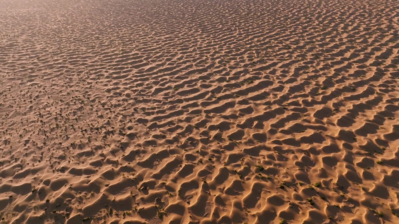 Aerial view of textured sand ripples and massive dunes in the Sahara Desert at sunset, capturing the vastness and orange glow of the Tunisian landscape