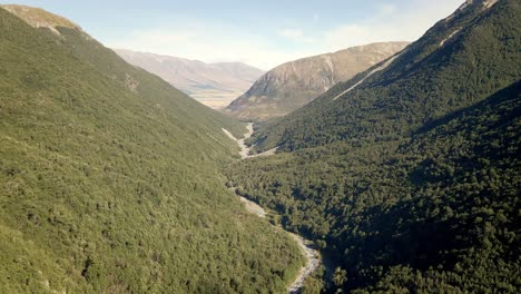 AERIAL---Creek-meandering-through-a-picturesque,-forested-canyon-in-warm-evening-sunlight