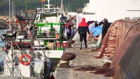 slow motion shot of fisherman walking with large fishing boats docked in puerto barbate