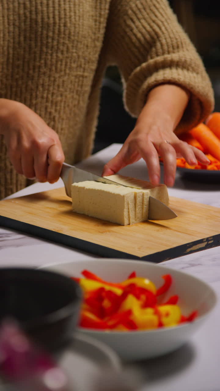 video vertical de primer plano de una mujer en casa en la cocina preparando una comida saludable vegetariana o vegana cortando tofu a bordo con un cuchillo 2