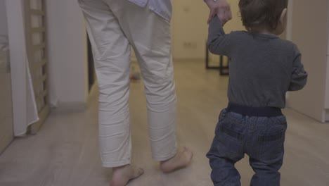 rear view of a mother helping her baby to take his first steps in the living room at home