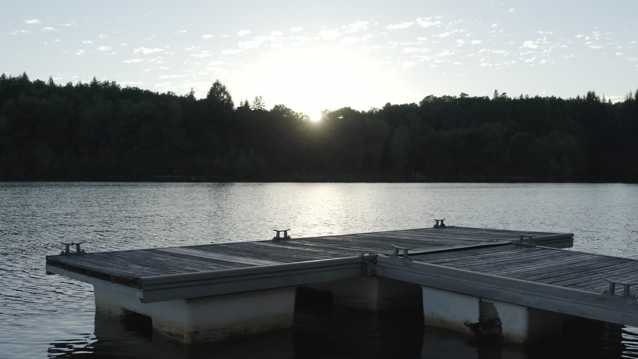 Aerial view flying over wooden boat dock on lake at sunset, sun reflecting on water, Marcillac La Croisille, France