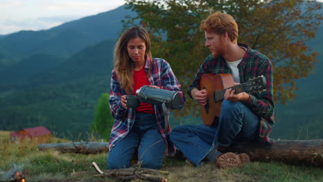 Family-couple-enjoy-mountains-on-camping.-Two-travelers-play-guitar-outdoors.