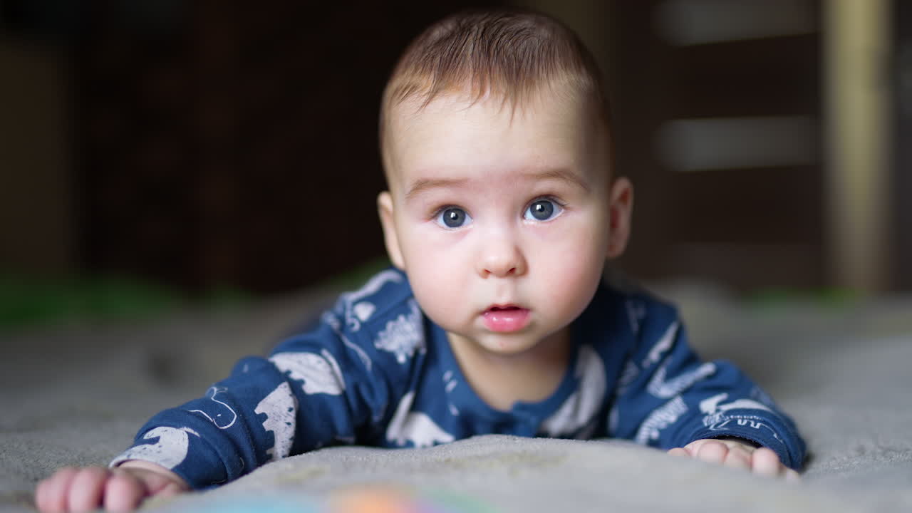Cute half-year old boy lies peacefully on the bed. Adorable child smiles sweetly to the camera. Blurred backdrop.