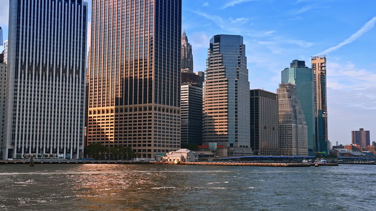 Nova Iorque, EUA, 1 de abril de 2026: Arranha-céus de Lower Manhattan refletidos na luz do East River. Horizonte da orla de Lower Manhattan com torres de vidro, superfície do rio e luz quente do fim de tarde