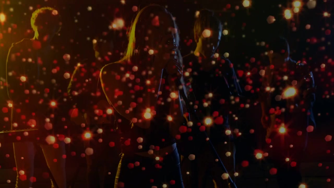 Camera opening singer moving to mic and singing to perform live, particle overlay pulsing over band