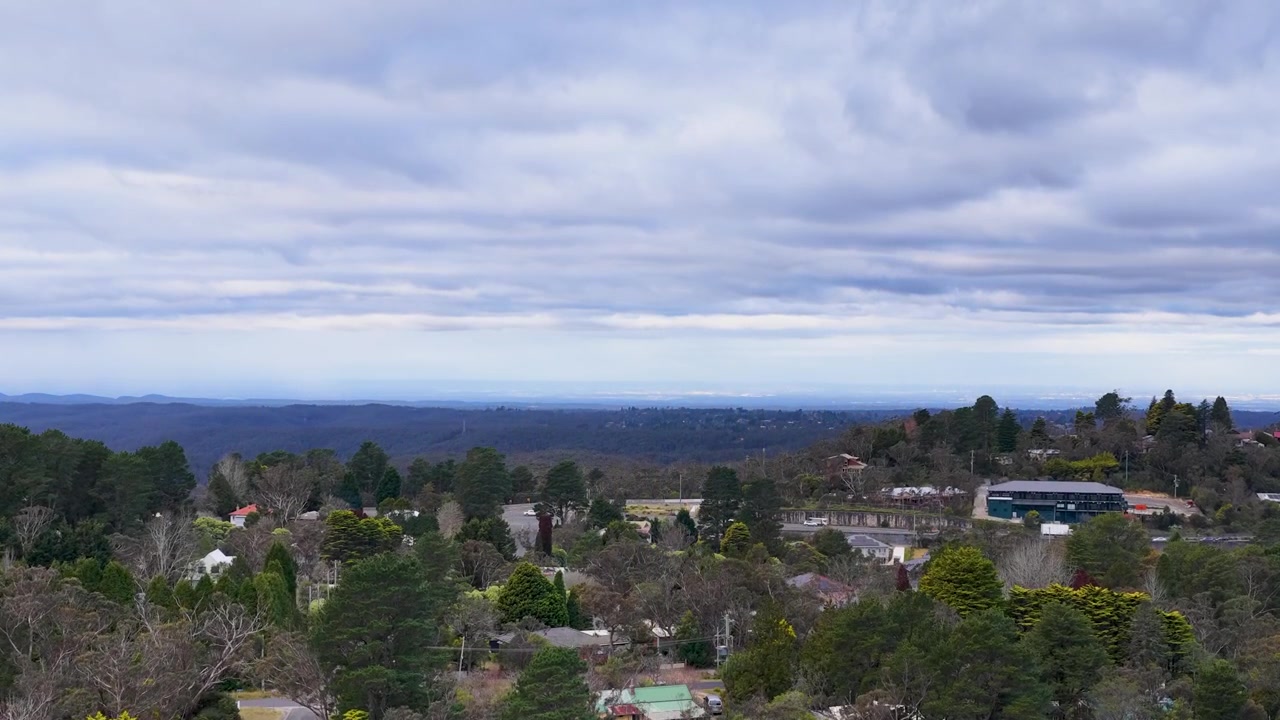 Il drone si muove su una boscaglia nativa di eucalipti verso una città di montagna residenziale sotto cieli nuvolosi