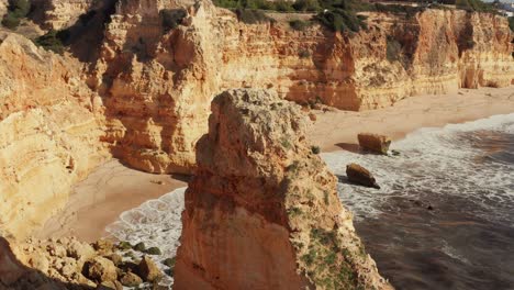 aerial tracking and tilitng shot of a limestone rock formation in the algarve region of portugal revealing a secluded white sand beach