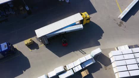 Aerial-view-of-a-semi-trucks-with-cargo-trailers-standing-on-warehouses-ramps-for-loading-unloading-goods-on-the-big-logistics-park-with-loading-hub