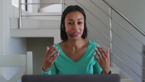 African-american-woman-wearing-phone-headset-talking-on-video-chat-on-laptop-while-working-from-home