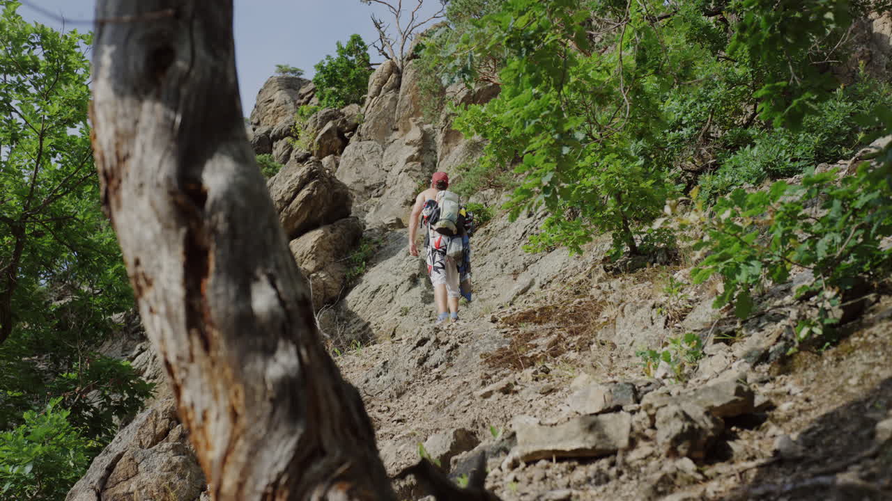 foto de atrás modelo hombre camina caminando por un sendero de montaña pecho desnudo, sombrero snapback, equipo de montañismo, escalada al aire libre, mirando a su alrededor para una pared para escalar, clima soleado de verano en austria, durnstein, europa