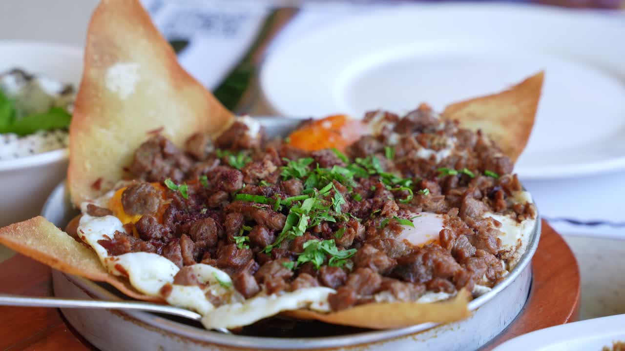 Savory skillet with spiced meat, fried eggs, crispy bread, and herbs—ideal for food content, Middle Eastern cuisine, brunch, or restaurant promo