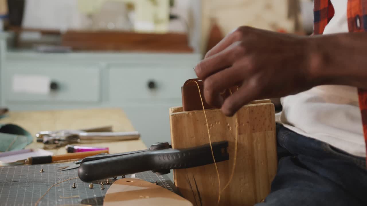 Hands of african american craftsman preparing wallet in leather workshop
