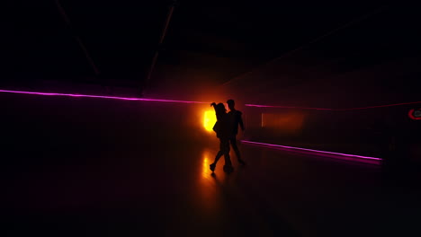 silhouettes of a couple moving at the music. dancers perform contemporary dance style in dark studio. yellow light lamp at backdrop.