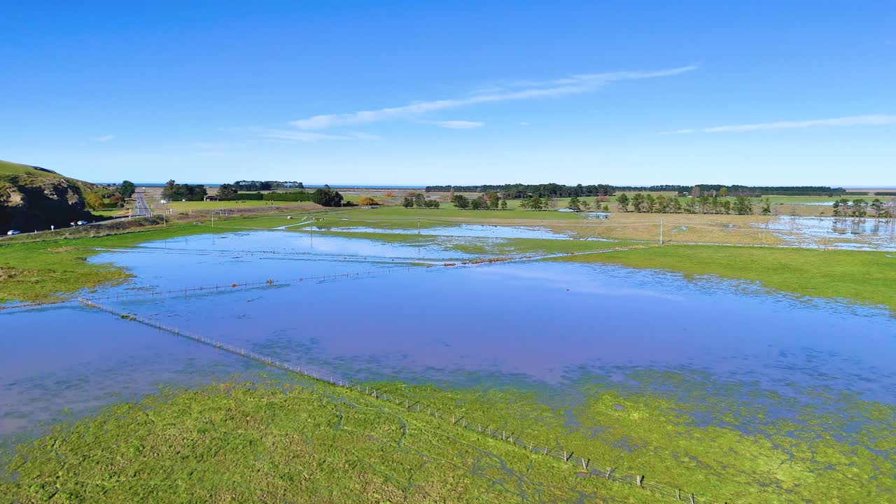 Aerial footage captures tranquil wetlands in Akaroa, New Zealand, under clear blue skies with vibrant green vegetation