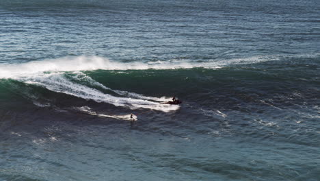 surfer on a rope behind a jet ski gets pulled onto a huge wave which he rides