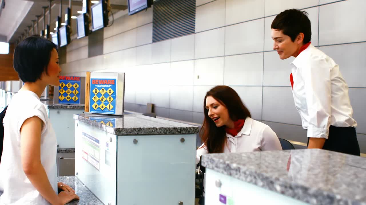 Dua staf bandara wanita memeriksa paspor dan bersama seorang wanita di meja check-in.