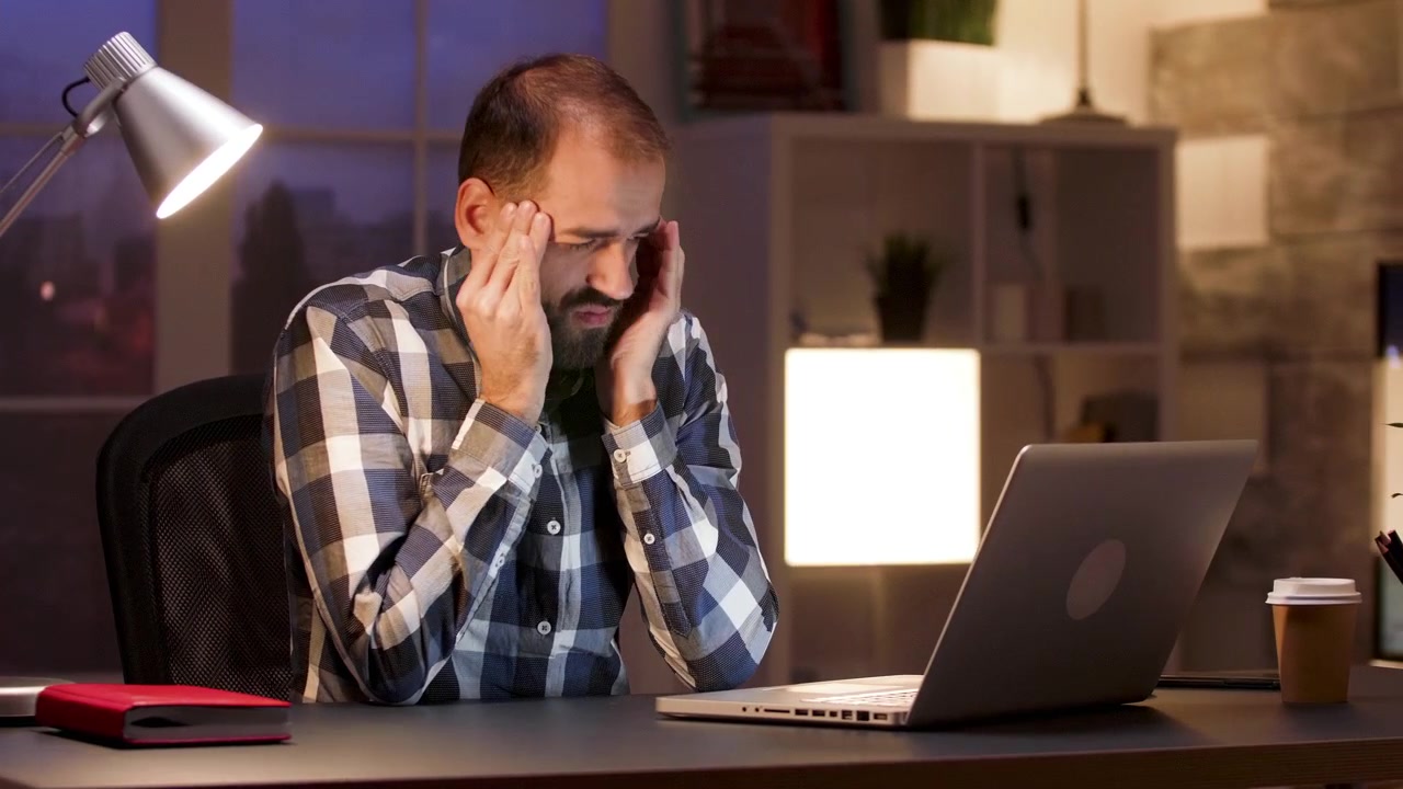 Stressed Man Working Late on Laptop in Office