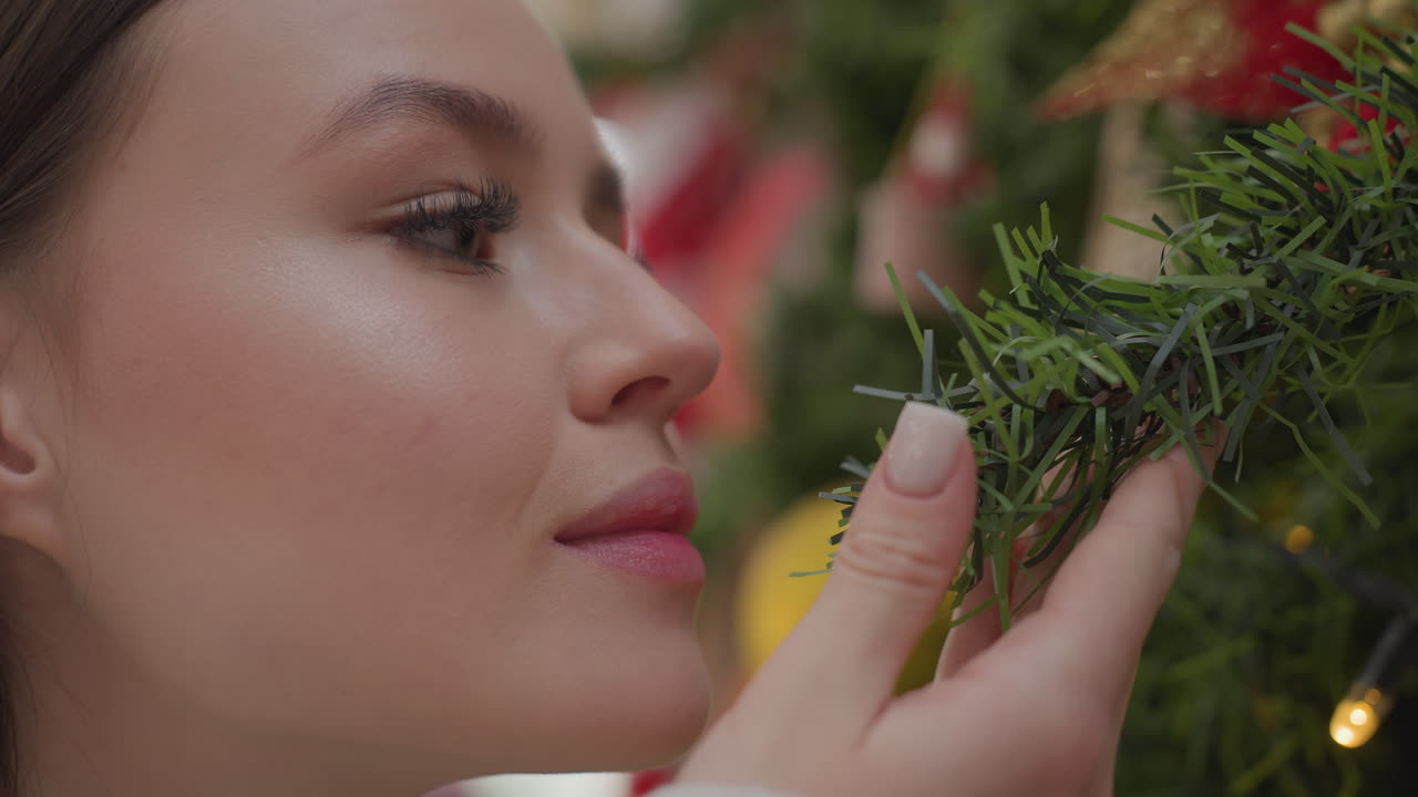 Close-up of white chic holding Christmas tree affectionately while smelling it, warm festive bokeh lights in background create a cozy, joyful holiday atmosphere filled with seasonal charm