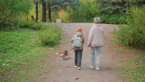 dog on leash sniffing ground beside leafy forest path under autumn foliage while mom and child walk ahead, casual stroll in nature, earthy tones and crisp seasonal atmosphere