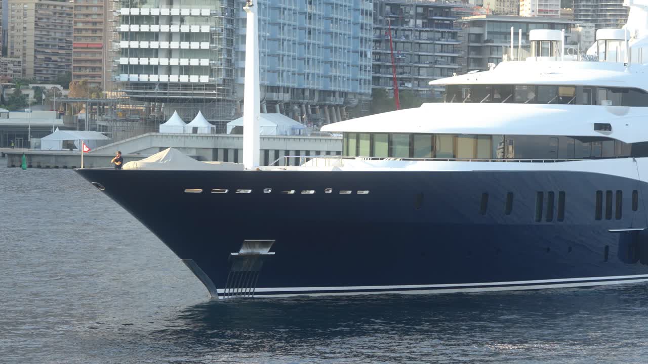 Luxury yacht anchored in Monaco's harbor with modern buildings in the background