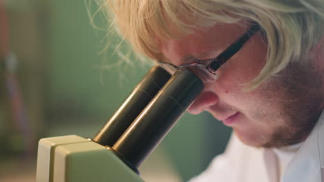 close-up view of a scientist with a blonde wig and glasses intensely examining a specimen through a microscope in a laboratory