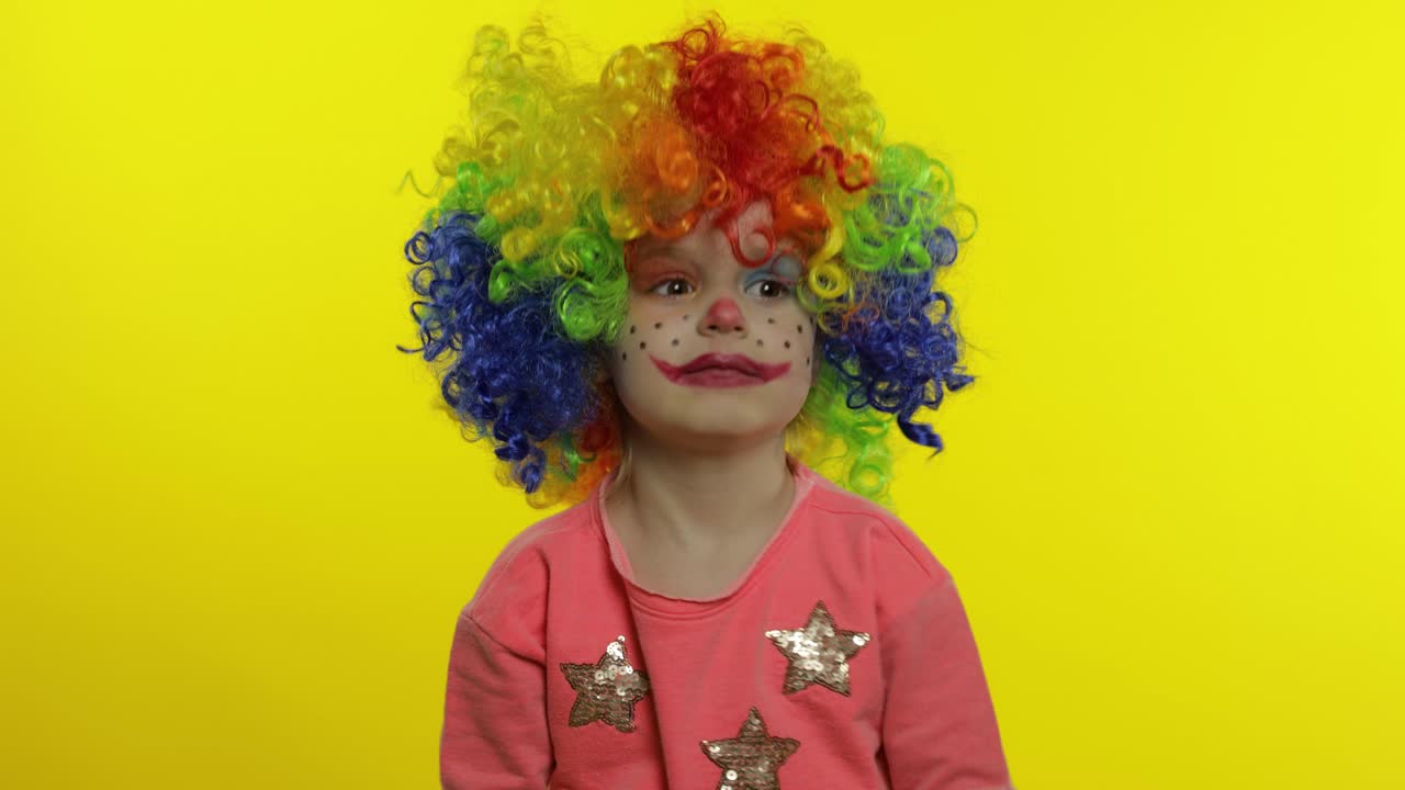 una pequeña niña payasa con una peluca colorida agitando las manos, divirtiéndose, sonriendo. halloween