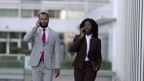 Two-confident-managers-walking-on-street-with-smartphones.