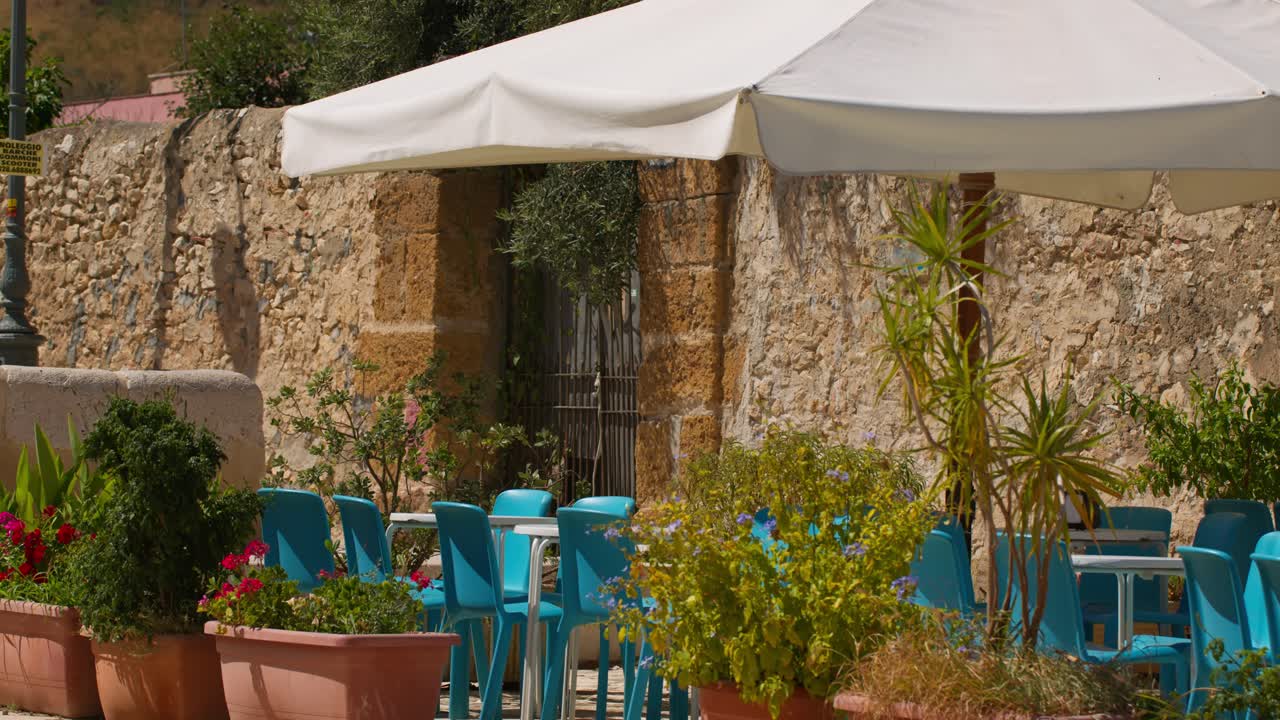 Scopello city center cafe with blue chairs, sunny exterior, Sicily, Italy