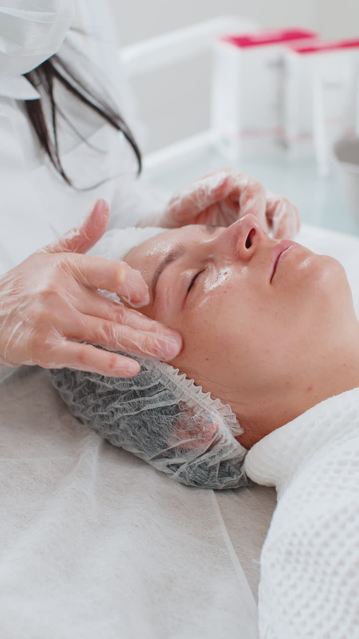 Terapista di cosmetologia che esegue un massaggio viso rilassante in una spa per una donna, con le mani, presso un salone detox e di benessere