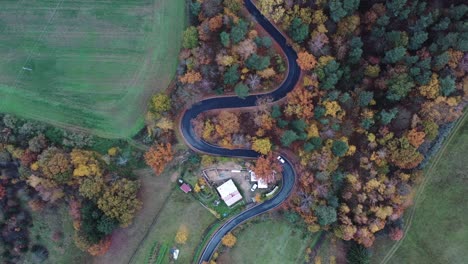 cinematic aerial view of lonely white car moving on curvy road, colorful autumn landscape of scenic valley, top down drone shot