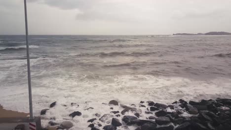 Aerial-drone-side-moving-shot,-kids-running-on-the-beach-on-bad-weather,-with-waves-crashing-on-the-beach-making-foam-on-an-overcast-day