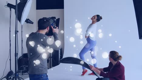 white spots floating against caucasian male photographer clicking pictures of female model at studio