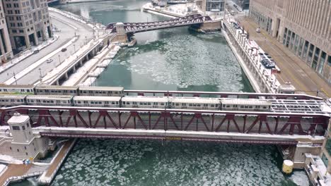 subway trains cross bridge above frozen chicago river in winter