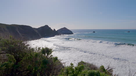 mountainside view of waves rolling in along the shores of big sur california beach, pacific ocean