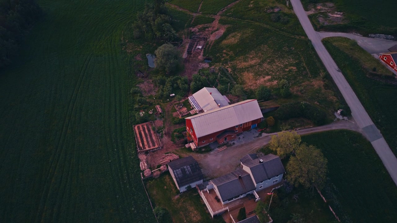 Fattoria norvegese con fienile rosso circondata da campi verdi al tramonto. - Ripresa aerea