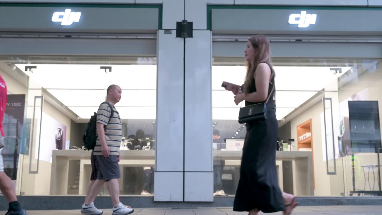 Low-angle shot of pedestrians walking past DJI's flagship store in Hong Kong, where the tech brand known for its drones and camera equipment draws a steady flow of customers.