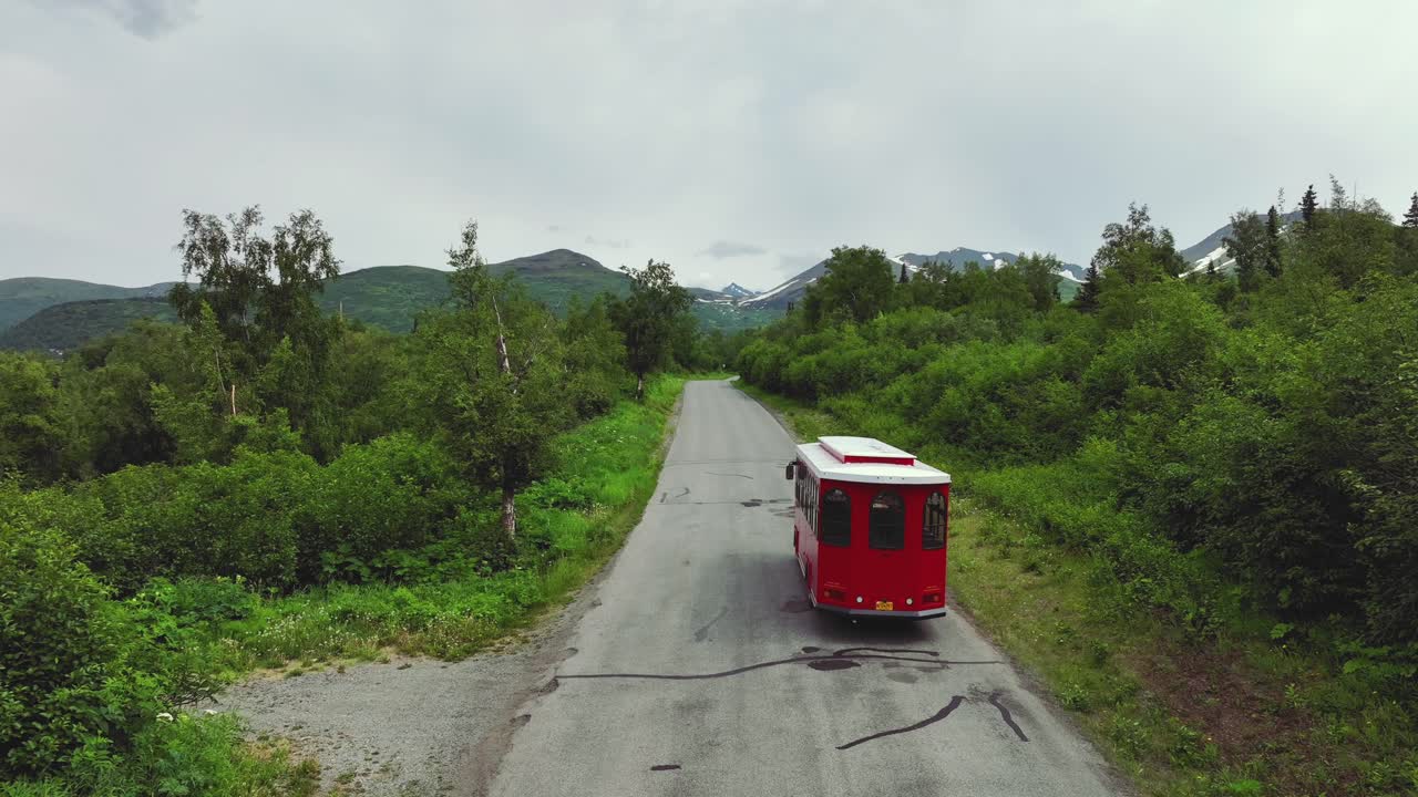 tranvía rojo conduciendo por una carretera rodeada de exuberante vegetación en alaska - seguimiento