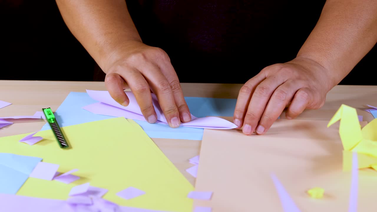 Person’s hands fold colored paper into origami, overhead view, bright lighting, stationary camera