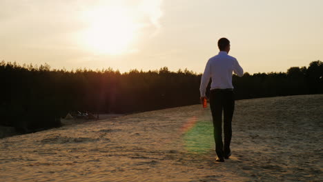 a businessman with a bottle of alcohol walks forward on the sand