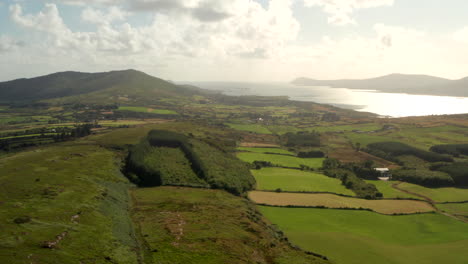 Toma-Aérea-Sobre-Tierras-Agrícolas-Rurales-Hacia-La-Montañosa-Costa-Irlandesa