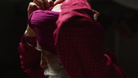 close up low key studio lighting shot of senior sikh man with beard tying fabric for turban against dark background 7