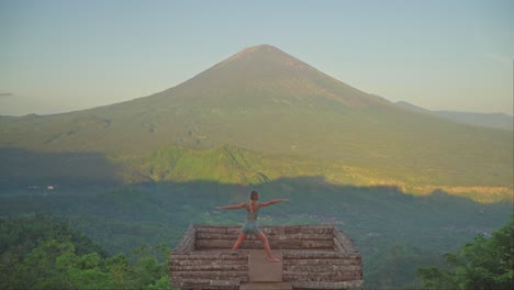 Mujer-Practicando-Pose-De-Guerrero-Feroz-Sobre-Una-Plataforma-De-Madera-Frente-Al-Monte-Agung